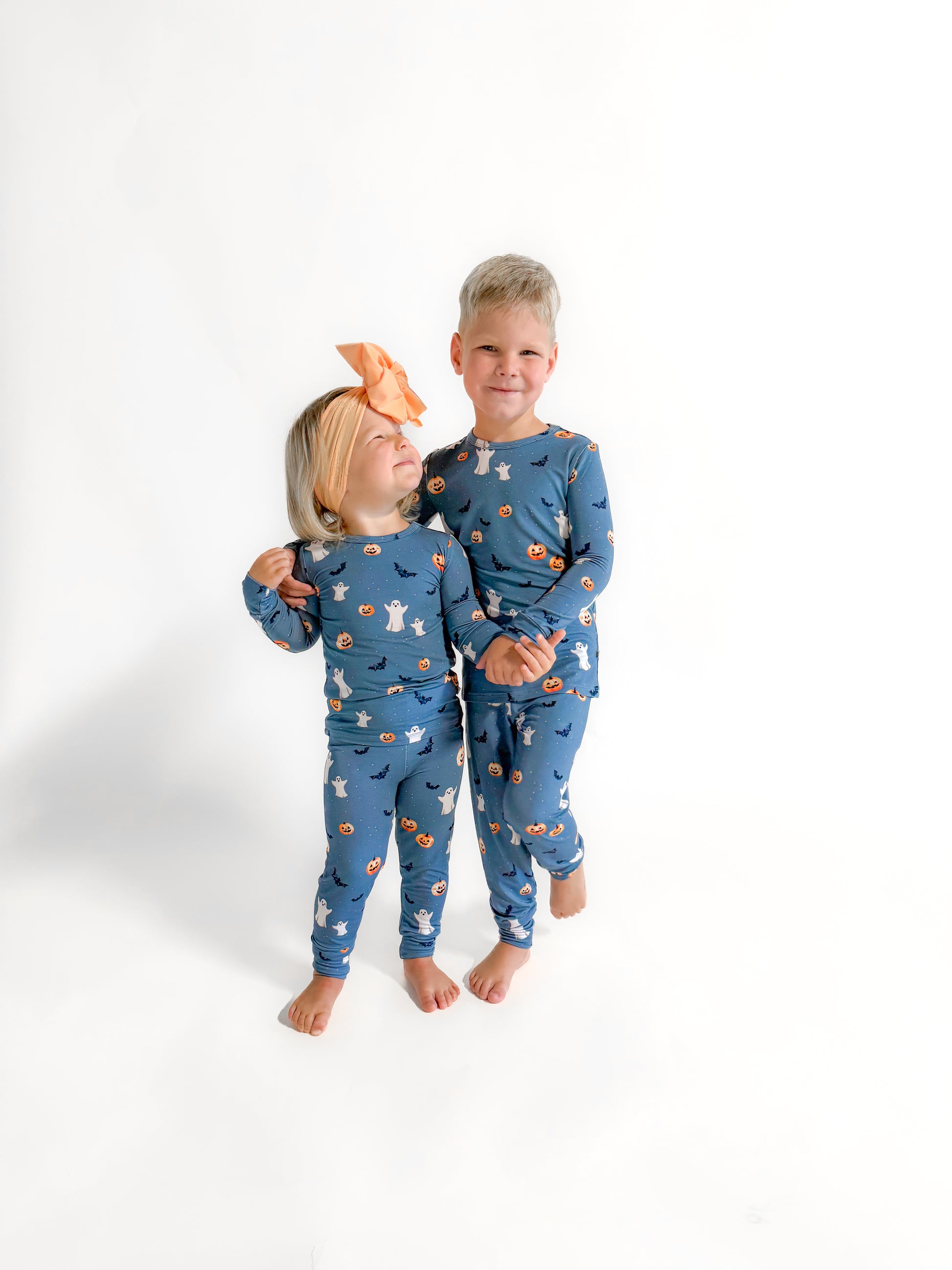 Two toddlers in soft bamboo Halloween pajamas featuring a festive print with pumpkins, ghosts, and bats, perfect for spooky season.