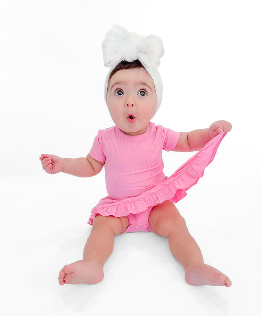 Baby girl sitting in a pink skirted bodysuit twirl dress made of soft ribbed bamboo fabric.