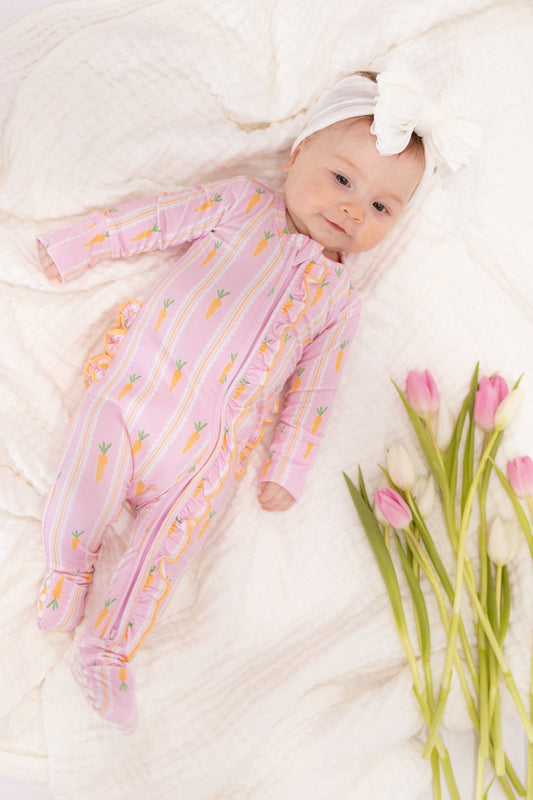 Baby in a pink Easter footie lying on a white blanket with tulips next to it