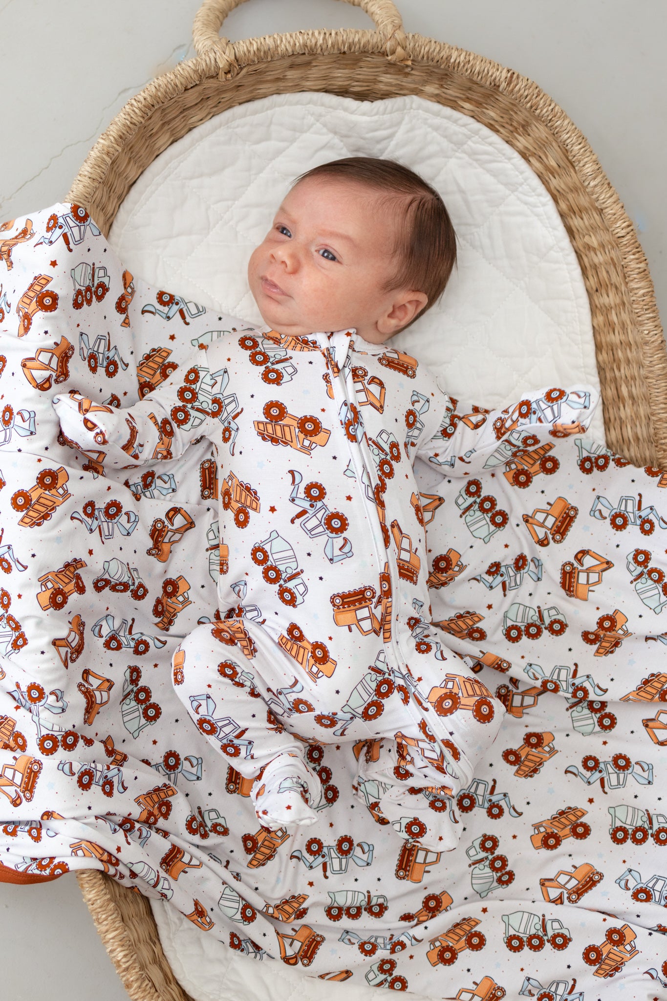 Newborn baby wrapped in a blanket with tractor pattern in a moses basket.