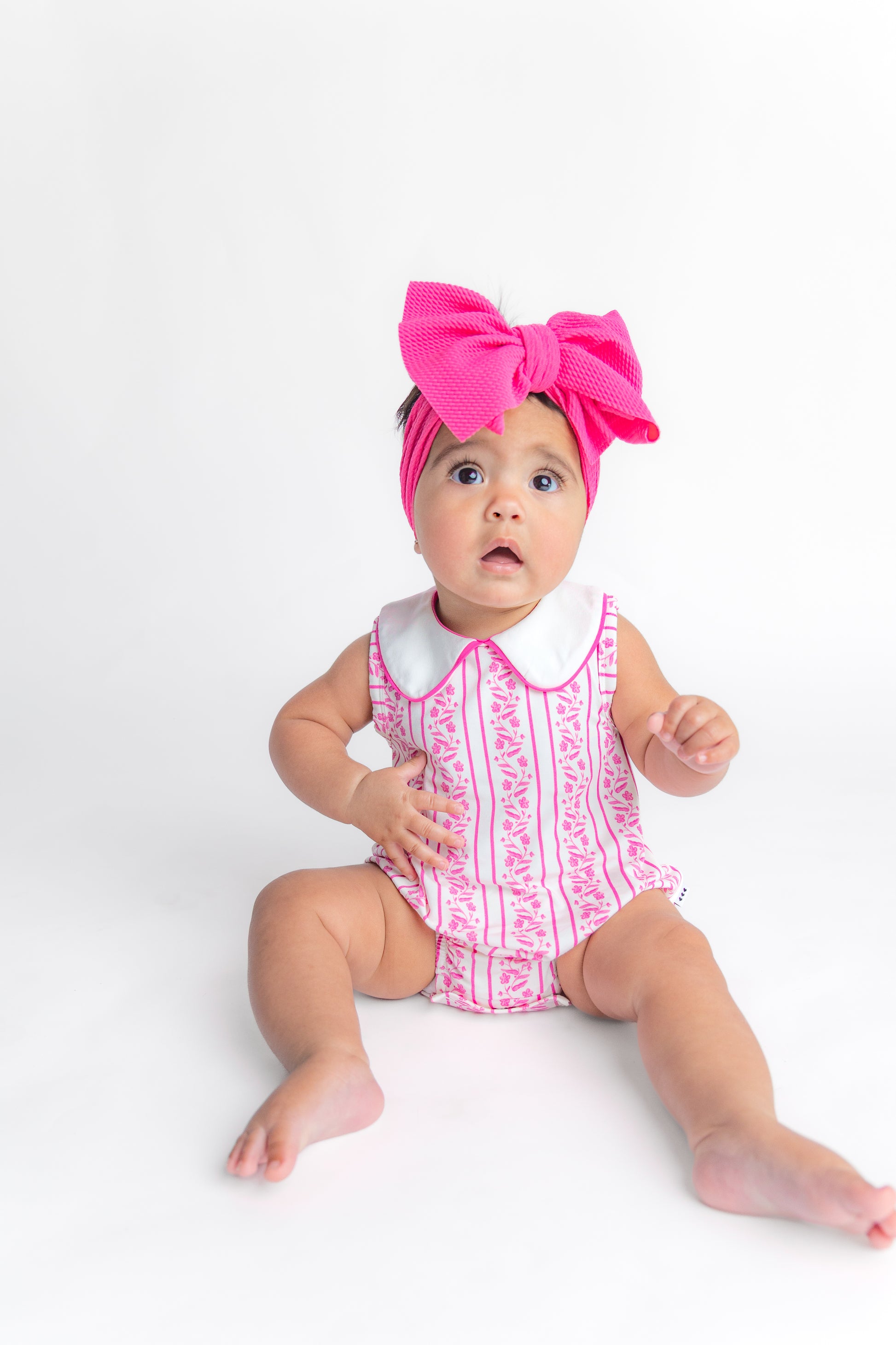 Baby girl wearing a hot pink headwrap bow and floral bubble romper.