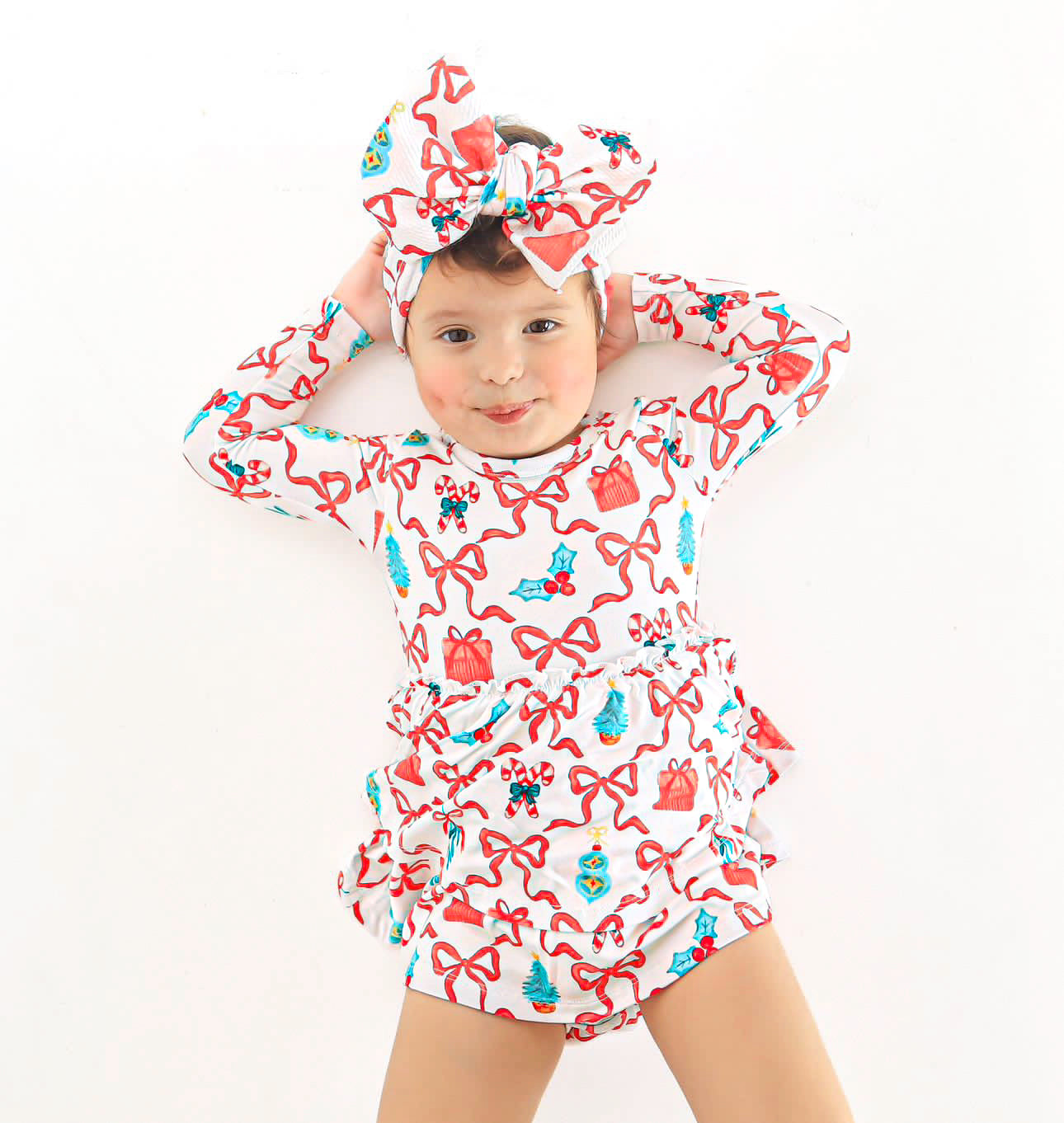 Adorable baby in a bamboo skirted bodysuit dress featuring a festive Christmas print of bows and candy canes, complete with a matching headwrap bow.