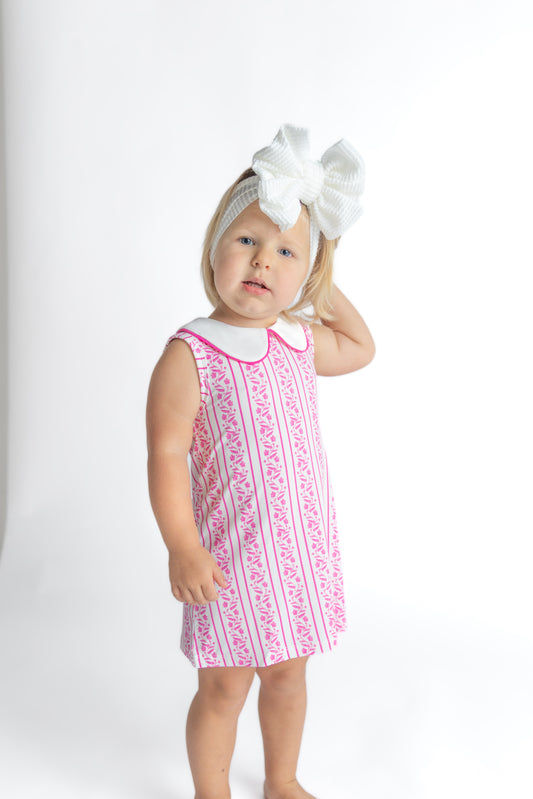 Young girl wearing a pink floral dress with a matching headband on a white background